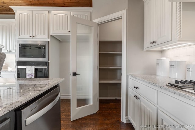 kitchen featuring tasteful backsplash, light stone countertops, built in microwave, dishwasher, and white cabinetry