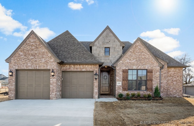 french country home featuring concrete driveway, a garage, brick siding, and a shingled roof