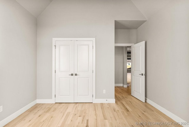 unfurnished bedroom with light wood finished floors, a closet, lofted ceiling, and baseboards