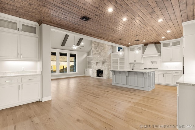 kitchen featuring a ceiling fan, premium range hood, lofted ceiling, white cabinetry, and a large fireplace