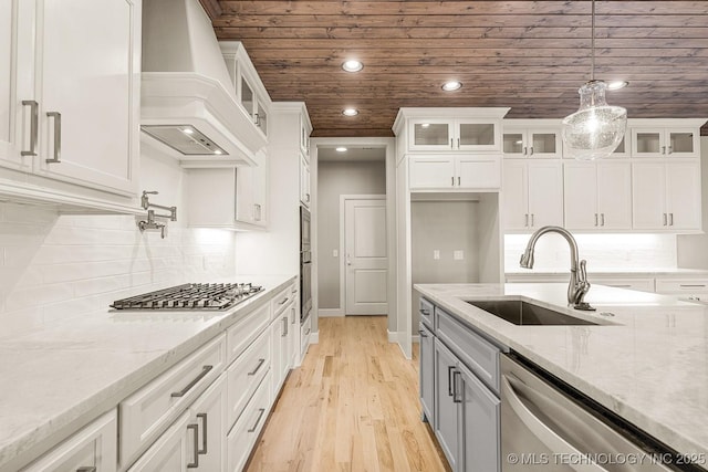 kitchen featuring custom range hood, stainless steel appliances, white cabinets, and a sink