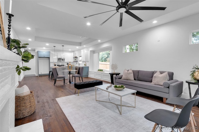 living area with dark wood finished floors, recessed lighting, a tray ceiling, and ceiling fan