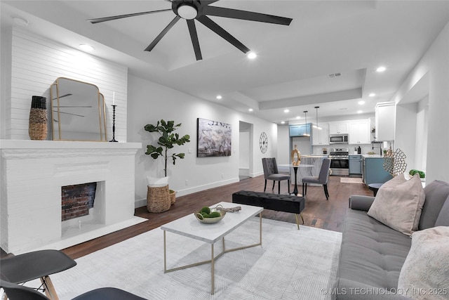 living area with visible vents, dark wood-type flooring, a tray ceiling, recessed lighting, and baseboards