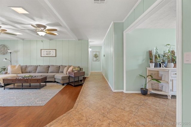 living room with tile patterned flooring, a ceiling fan, visible vents, and a textured ceiling