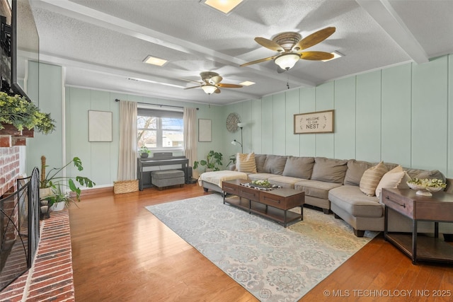 living area with beam ceiling, a textured ceiling, wood finished floors, a fireplace, and a decorative wall