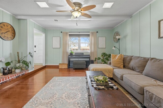 living room featuring beamed ceiling, a ceiling fan, a textured ceiling, wood finished floors, and crown molding