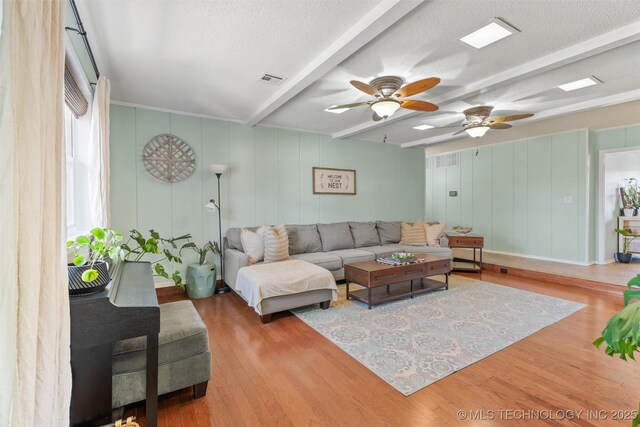 living room with beamed ceiling, a textured ceiling, visible vents, and wood finished floors