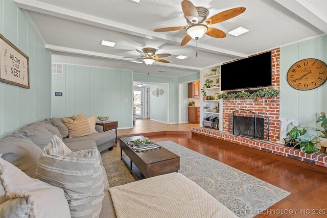 living area featuring visible vents, light wood-style flooring, a fireplace, beamed ceiling, and a decorative wall