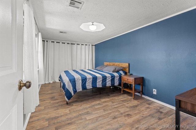 bedroom with wood finished floors, visible vents, and a textured ceiling