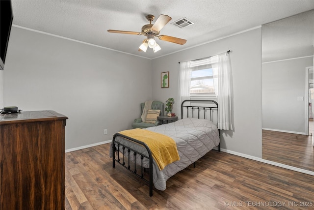 bedroom featuring wood finished floors, baseboards, visible vents, ornamental molding, and a textured ceiling