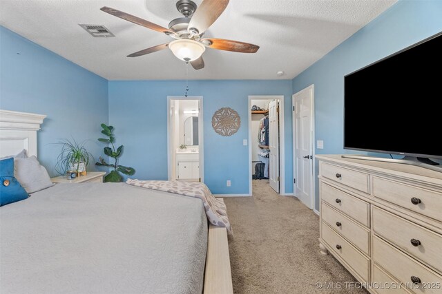 bedroom with a spacious closet, visible vents, connected bathroom, light carpet, and a textured ceiling