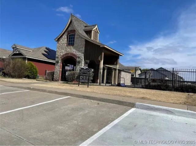 exterior space featuring stone siding, uncovered parking, and fence