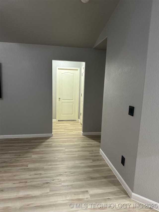 unfurnished room featuring lofted ceiling, baseboards, and light wood-type flooring