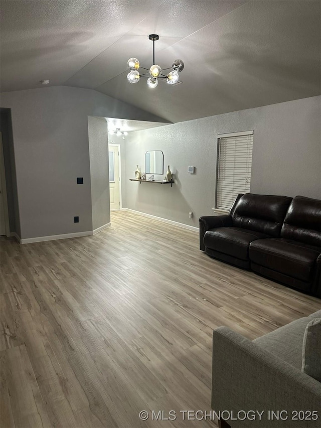 living room featuring a notable chandelier, light wood-style flooring, a textured ceiling, and lofted ceiling