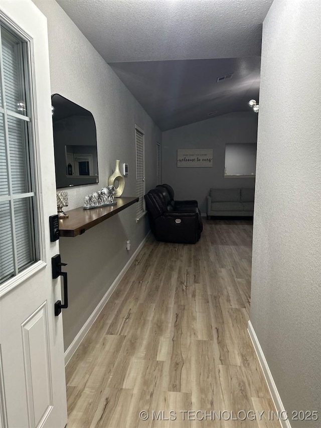 corridor with vaulted ceiling, baseboards, visible vents, and wood finished floors