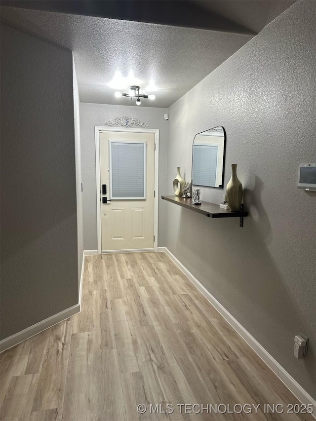 doorway featuring baseboards, a textured ceiling, light wood-style flooring, and a textured wall