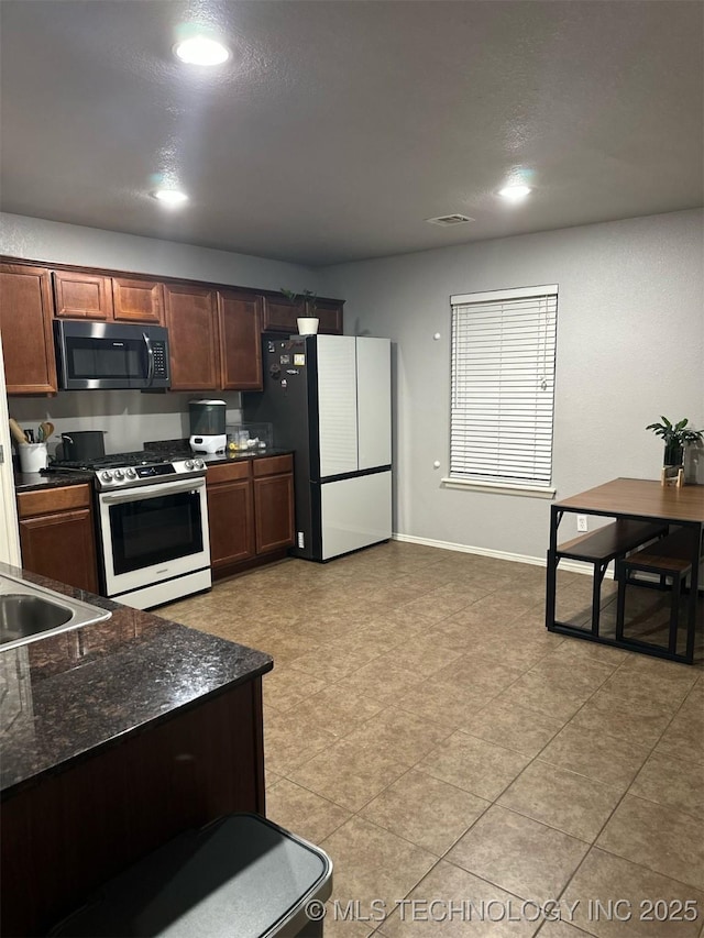 kitchen with visible vents, baseboards, stainless steel range with gas stovetop, dark stone counters, and freestanding refrigerator