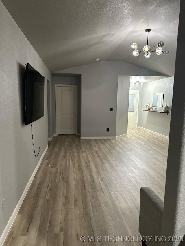 unfurnished living room featuring baseboards, a textured ceiling, wood finished floors, and vaulted ceiling