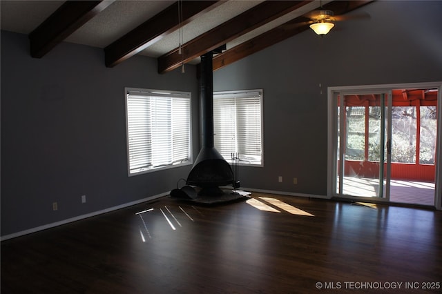 empty room with baseboards, vaulted ceiling with beams, wood finished floors, and a wood stove