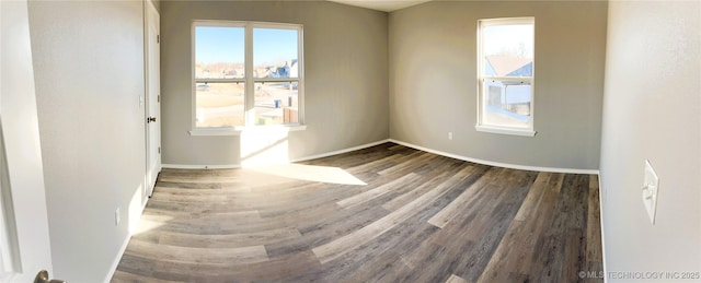 spare room with plenty of natural light, wood finished floors, and baseboards