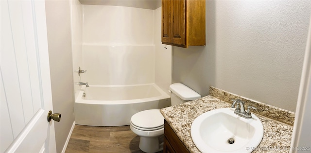 full bath with vanity, wood finished floors, shower / tub combination, toilet, and a textured wall