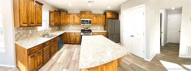 kitchen featuring visible vents, a kitchen island, a sink, stainless steel appliances, and brown cabinets