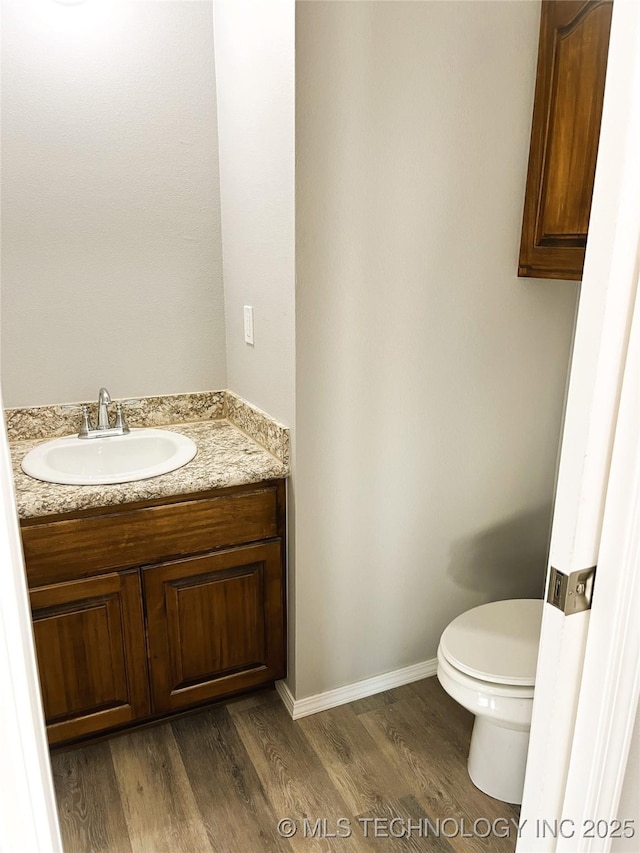 half bathroom featuring vanity, toilet, wood finished floors, and baseboards