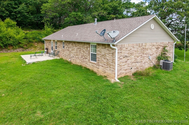 rear view of property featuring brick siding, roof with shingles, a lawn, cooling unit, and a patio