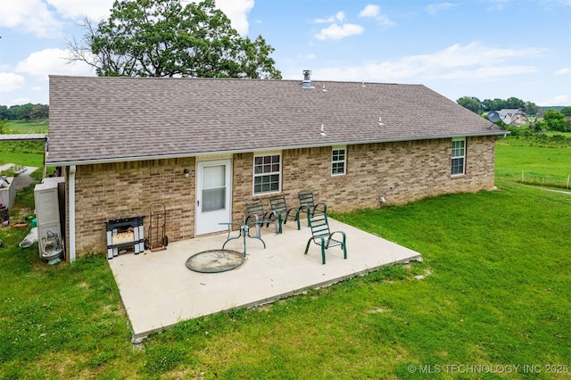 back of house with brick siding, a patio area, a lawn, and roof with shingles