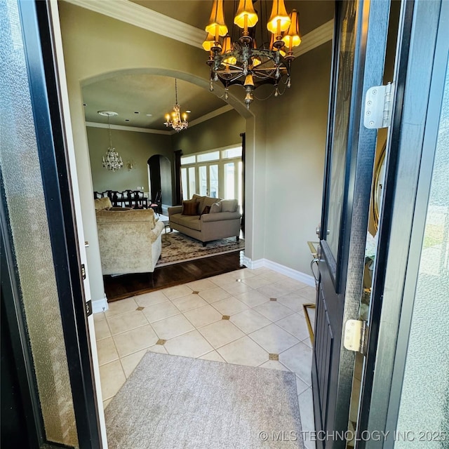 foyer featuring a notable chandelier, ornamental molding, arched walkways, light tile patterned floors, and baseboards