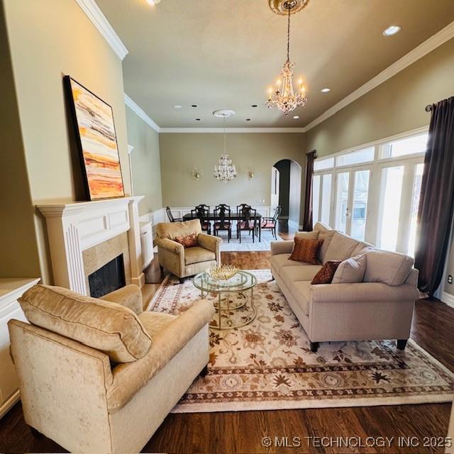 living area featuring wood finished floors, arched walkways, a fireplace, crown molding, and a chandelier