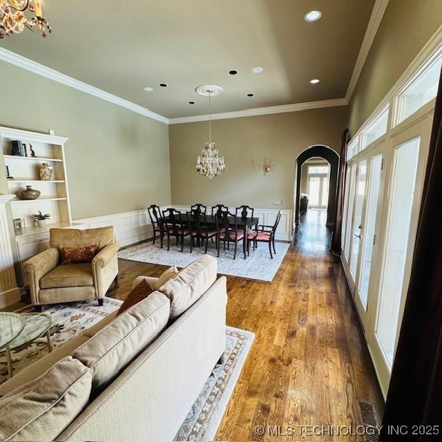 living area with ornamental molding, recessed lighting, an inviting chandelier, wood finished floors, and arched walkways