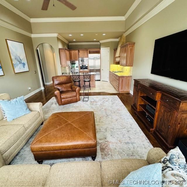 living area featuring arched walkways, a ceiling fan, baseboards, and wood finished floors