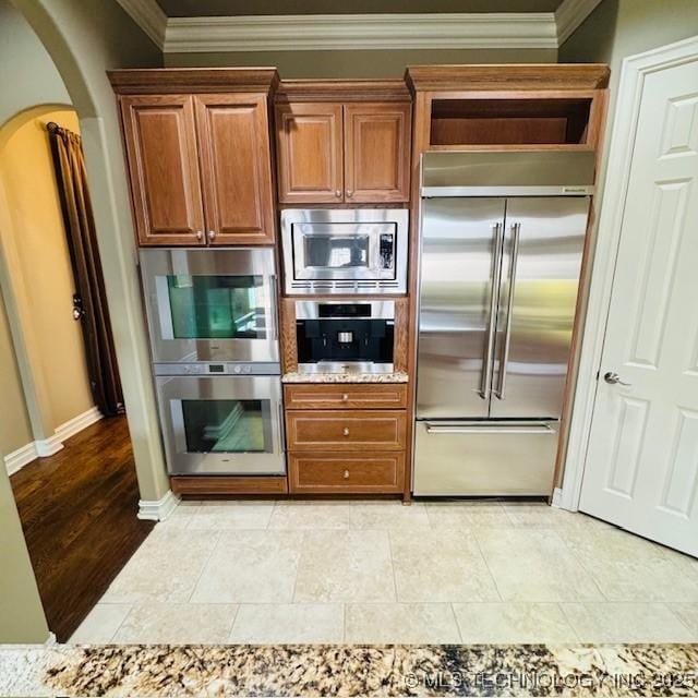 kitchen with brown cabinetry, baseboards, arched walkways, built in appliances, and crown molding