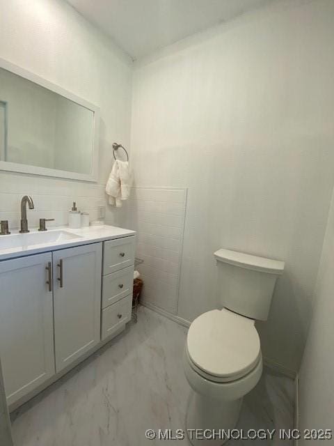 half bathroom with marble finish floor, vanity, tile walls, and toilet