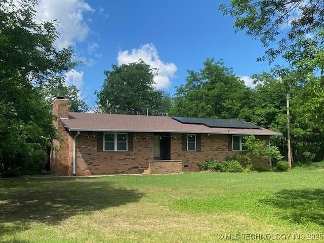 ranch-style home featuring solar panels, a front lawn, brick siding, and a chimney