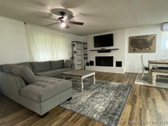 living area featuring a wall unit AC, a brick fireplace, ceiling fan, and wood finished floors