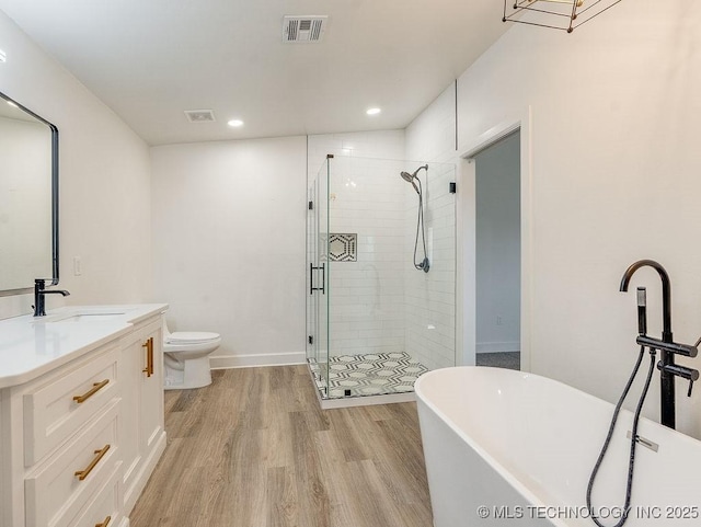 bathroom featuring visible vents, wood finished floors, a shower stall, a freestanding bath, and vanity
