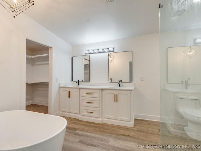 full bathroom featuring toilet, a sink, wood finished floors, double vanity, and a spacious closet