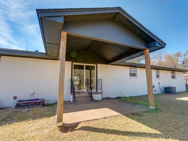 entrance to property with brick siding, central air condition unit, a patio area, a lawn, and crawl space
