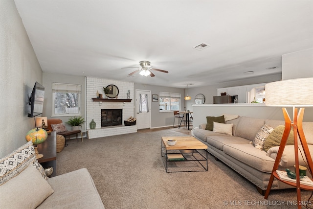 carpeted living room with visible vents, plenty of natural light, a brick fireplace, and a ceiling fan