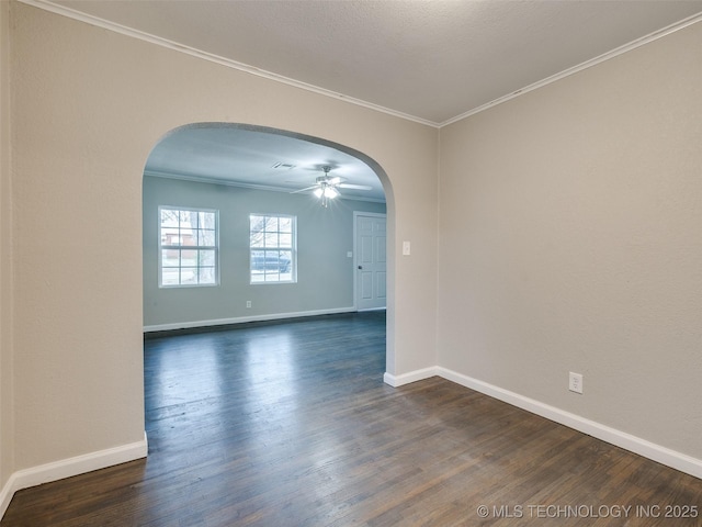 empty room featuring arched walkways, dark wood finished floors, crown molding, and baseboards