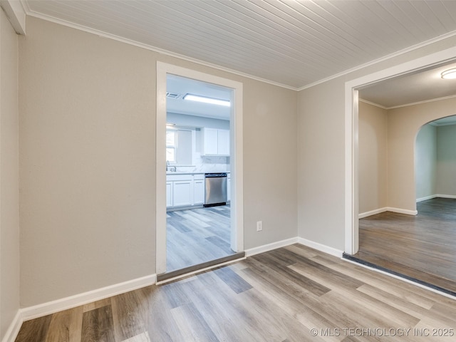 unfurnished room featuring arched walkways, ornamental molding, baseboards, and wood finished floors