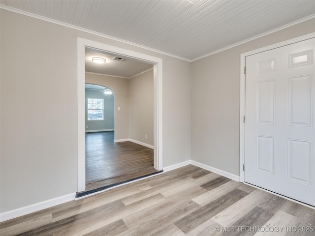 empty room with crown molding, wood finished floors, visible vents, and arched walkways