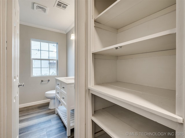 bathroom featuring visible vents, toilet, wood finished floors, and ornamental molding