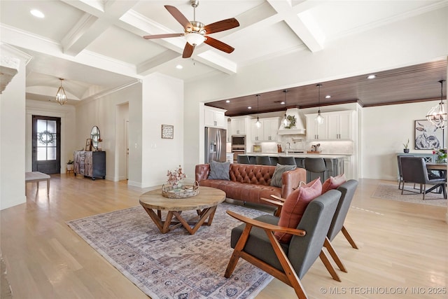 living area featuring beam ceiling, coffered ceiling, light wood-style flooring, and ceiling fan with notable chandelier