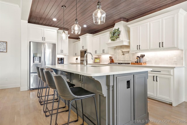 kitchen featuring a center island with sink, a sink, decorative backsplash, stainless steel appliances, and wood ceiling