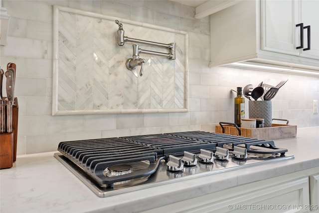 details with decorative backsplash, light countertops, stainless steel gas stovetop, and white cabinetry