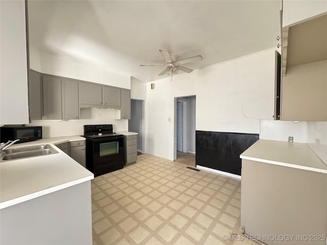 kitchen with gray cabinetry, light floors, light countertops, black appliances, and a sink