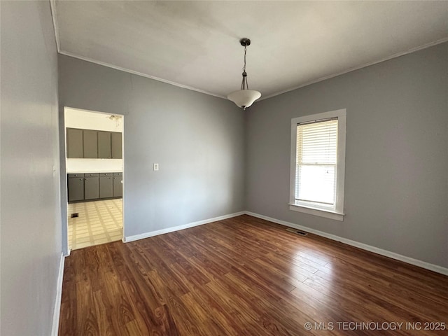 spare room featuring dark wood finished floors, crown molding, baseboards, and visible vents